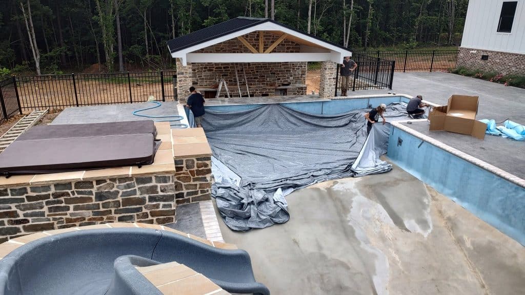 Construction workers installing pool liner in new inground pool.
