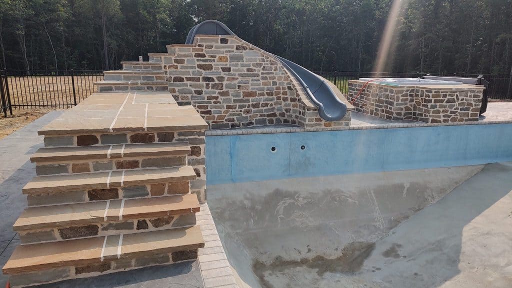 Stone water slide with poolside stonework and stairs.